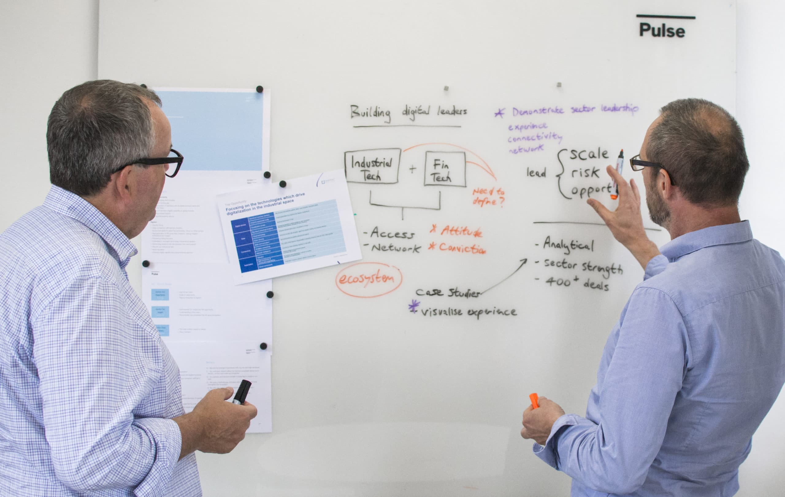 Two men looking at a whiteboard with diagrams
