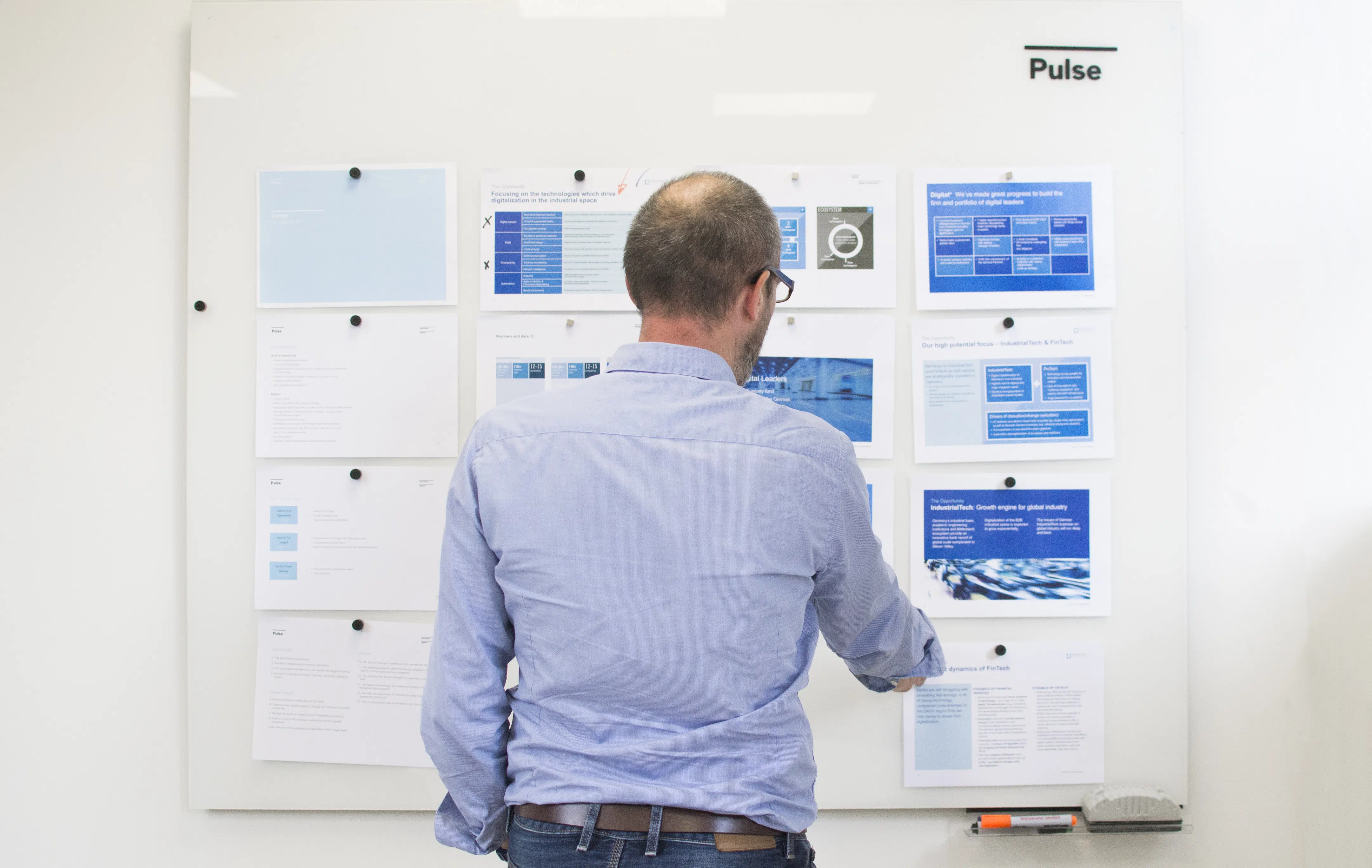 Man with blue shirt looking at white board with blue and white pieces of paper